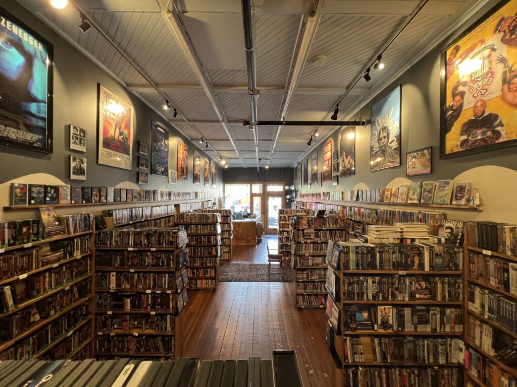 Picture of a video store facing the front door. Shelves of videos and dvds on the left and right.